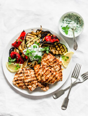 Delicious tapas barbecue set - grilled turkey, aubergine, zucchini, bell pepper with tzatziki sauce on a light background, top view