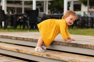Cute smiling baby girl in yellow dress playing on the steps. Outdoors. The concept of a happy...