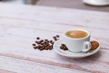 Cup of coffee with beans on a light wooden table.