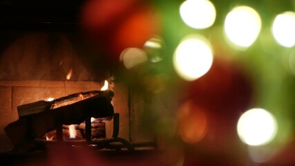 Christmas tree lights by fire in fireplace, New Year or Xmas decoration of pine or fir with red balls. Fireside on winter christmastime holiday. Cozy place by firewood. Seamless looped cinemagraph.
