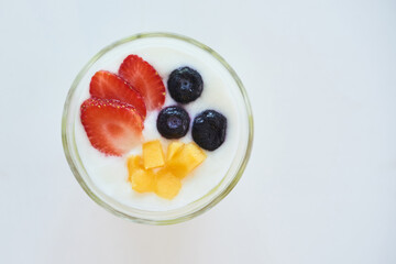 Glass of fresh yogurt with strawberries, blueberries and mango on white table, view from the top