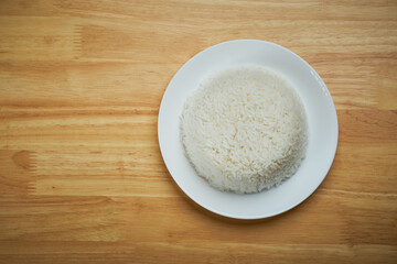 flat lay top view shot of streamed white Thai's jasmine rice in the white clean dish isolated put on the wooden plate dinner table closed to one conner of the photo with empty copy space for texts