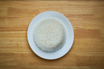 flat lay top view shot of streamed white Thai's jasmine rice in the white clean dish isolated put at the center of the wooden plate dinner table