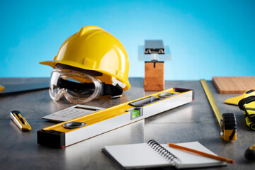 Contractor concept. Tool kit of the contractor: yellow hardhat and libella on the gray tiles and on the blue background.