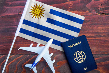 Flag of Uruguay with passport and toy airplane on wooden background. Flight travel concept 