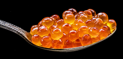 Silver spoon of red caviar on black background. Macro picture.