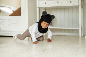 Adorable african american little boy in hat helmet with two fluffy bobbles crawling on floor of...
