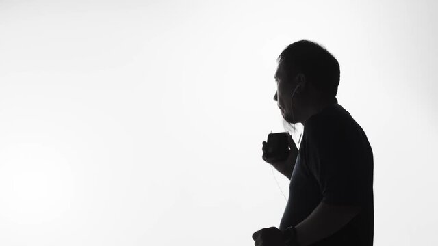 Silhouette of a man listening to music on a smartphone, vintage tape player or smart device