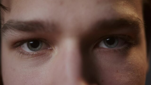 Portrait of young sad man with light blue gray eyes, looking in camera with joyless, sorrowful view. Close-up of male face student.