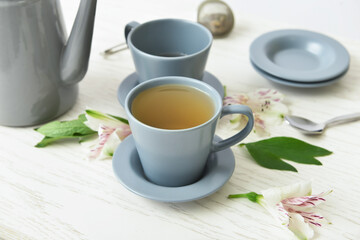 Cups of floral tea and flowers on light wooden background