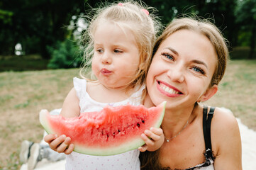 Cute daughter with mother eating watermelon in the summer. Happy girls in the park.