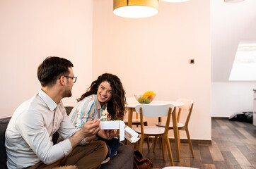 Smiling couple sitting on sofa and eating fast food salad at home.