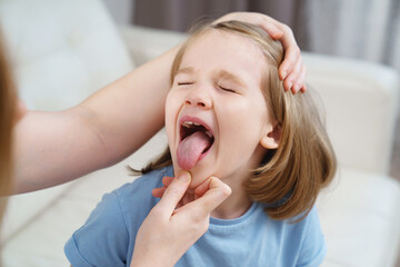 the little girl complains of a sore throat and her mother examines it. 