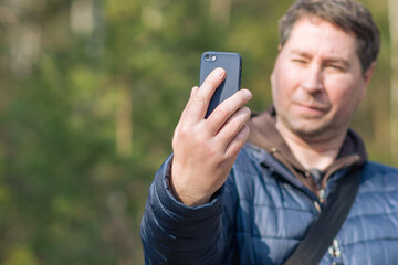 One 40s man with his mobile smart phone searching for reception signal in the forest.