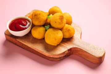 Board with fried potato balls and sauce on color background