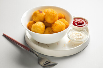 Bowl with fried potato balls on light background