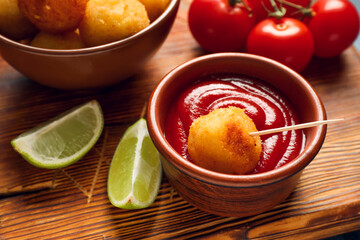 Bowl with tomato sauce and fried potato ball on board