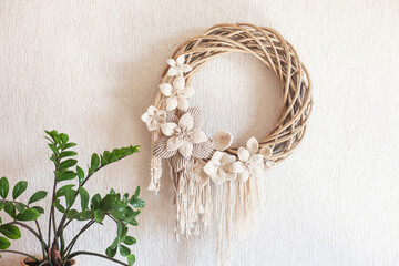 Macrame wreath with big cotton flower on a white decorative plaster wall. Natural cotton thread and...
