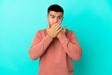 Young handsome man over isolated blue background covering mouth with hands