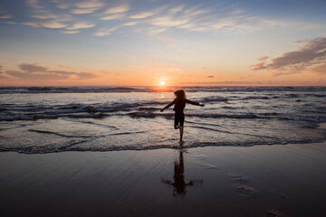 young girl running and jumping with happiness on the beach at sunset