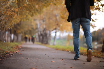 Autumn concept. Pedestrian feet on the road. Autumn leaves on the footpath.
