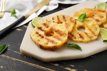 Board with grilled pineapple slices and lime on dark wooden background, closeup