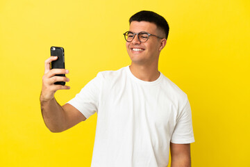 Young handsome man over isolated yellow background making a selfie