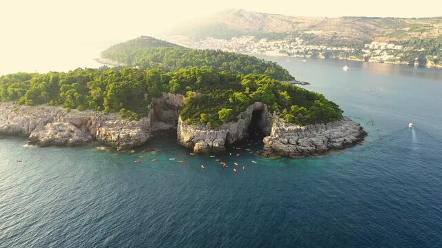 Aerial footage of the Lokrum Island and a group of tourists on a kayak tour and a boat passing by, Dubrovnik , Croatia