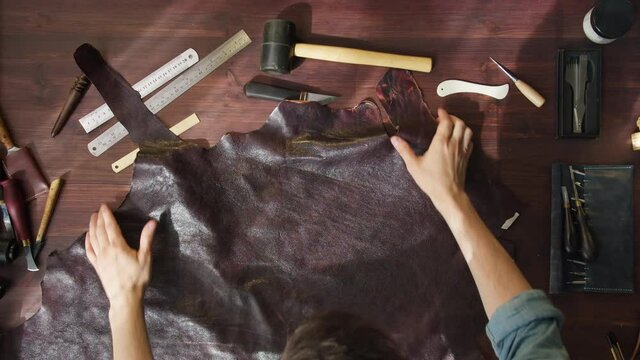 Throwing dark brown leather on table, preparing materials and tools before working. Putting fragment of cowhide on workplace, making handmade products made of genuine or artificial leather.