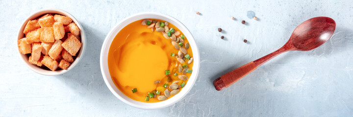 Spicy pumpkin soup panorama with croutons, overhead flat lay shot with a wooden spoon