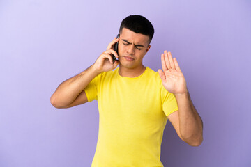 Young handsome man using mobile phone over isolated purple background making stop gesture and disappointed