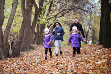 Naklejka premium Young family on a walk in the autumn park on a sunny day. Happiness to be together.