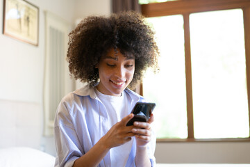 Satisfied hipster girl with Afro haircut, types text message on cell phone, enjoys online communication, types feedback