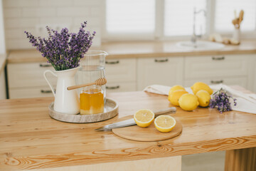Fresh lemons, jar with honey and bunch of lavender flowers in a vase standing on a kitchen table at home. Ingridients for making lemonade.