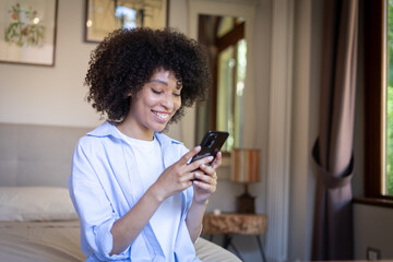 Satisfied hipster girl with Afro haircut, types text message on cell phone, enjoys online communication, types feedback