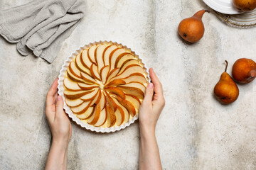 Woman's handbody, holding a homemade raw pie with fresh  brown pears, before baking. Light...