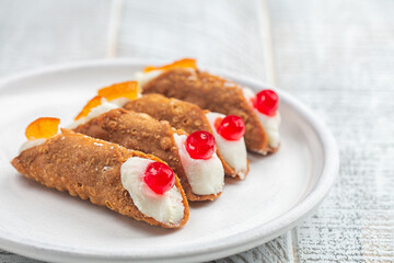 Close-up of Sicilian pastry cannoli with ricotta cheese cream topped with cherries. White wood surface.