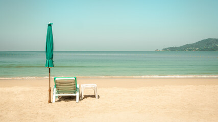White plastic beach chair, table and green umbrella on tropical sand beach by the sea in summer of Phuket, Thailand in pastel color tone. 