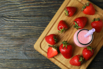 Bottle of strawberry milkshake and ingredients on wooden table