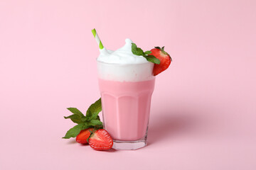 Glass of strawberry milkshake and ingredients on pink background
