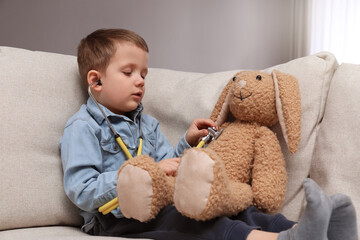 Cute little boy playing with stethoscope and toy bunny at home. Future pediatrician