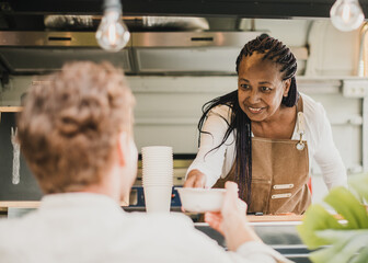 African chef woman serving take away order inside food truck - Focus on senior woman face - Powered by Adobe
