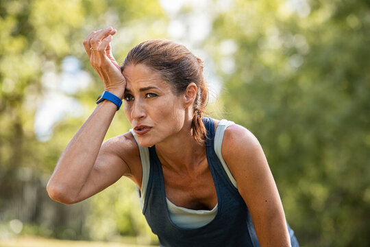 Tired mature runner wiping sweat after workout at park