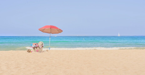 Bag on the beach with umbrella and vacation objects, blue sea and tropical sun. Concept: vacation at sea