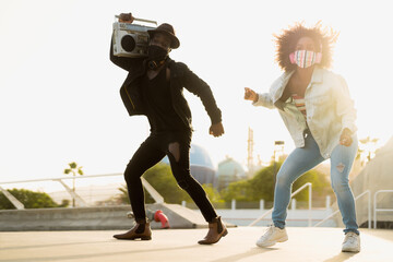 Young Afro friends dancing outdoor while listening to music with wireless headphones and vintage boombox