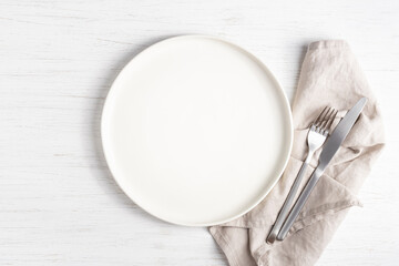 White empty plate and silver cutlery on linen napkin.