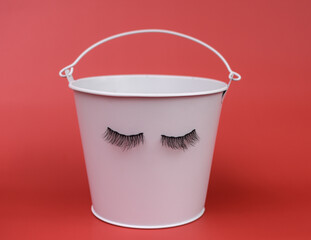 a white bucket with false eyelashes on a red background. Lashmaker. magnetic eyelashes on metal. the concept.