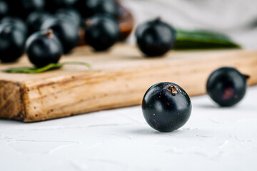 Black currant on a wooden board on a white concrete table