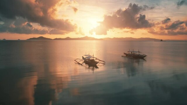 Aerial pink sunset is reflected on surface sea. National Filipino boats on dark water, golden hour. Beautiful tropical landscape, walk in Bangk, natural light. Popular tourist destination. Philippines
