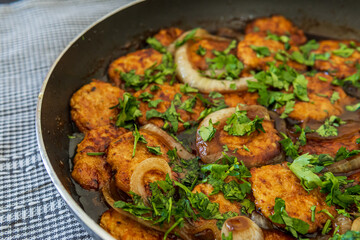 Sweet and sour chicken patties in a pan on a plaid towel, ready to be served. Chicken cutlets cooked with Asian flavored sauce, onions, and parsley. Chinese style dish, selective focus, vibrant colors